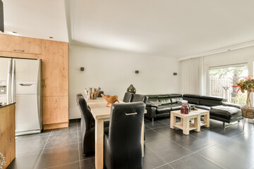 A sleek modern kitchen featuring wooden cabinetry and a cozy dining space with black chairs, inviting natural light from large windows.