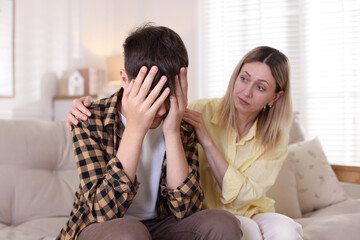 Mother consoling her upset son on sofa at home
