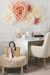 Beautiful decorative paper flowers on white wall and stylish furniture indoors