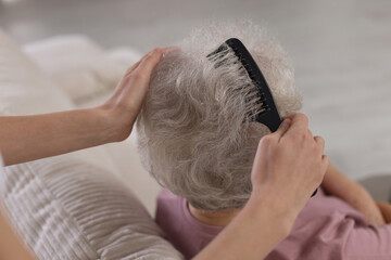 Woman brushing senior lady with comb indoors, closeup