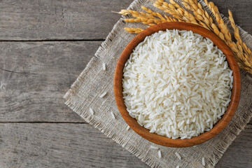 White rice filling wooden bowl on rustic table, complemented by delicate stalks