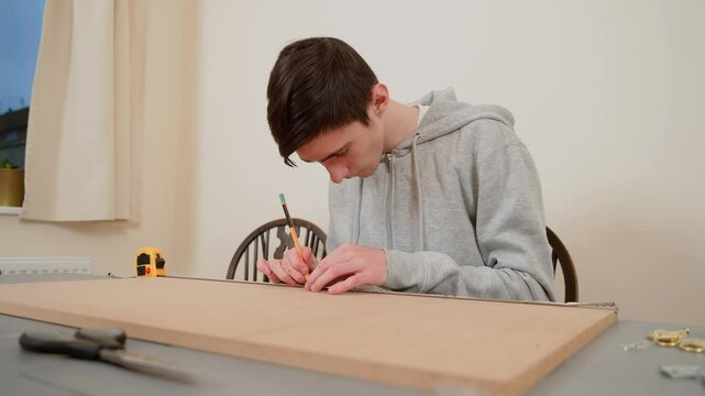Boy concentrating on marking lines on wooden board with pencil. Male student working on design project in organized workplace. Precision and attention to detail vital for successful construction