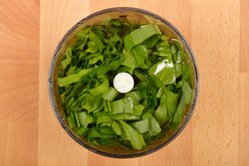 Chopped fresh wild garlic (Allium ursinum) leaves are in a food processor bowl on a wooden surface,...