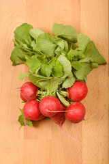 A bunch of fresh, vibrant red radishes with green leaves rests on a light wooden surface, captured in a close-up, top-down shot