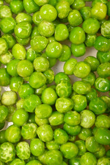 A close-up, top-down shot shows a dense pile of fresh, vibrant green peas, some glistening with moisture