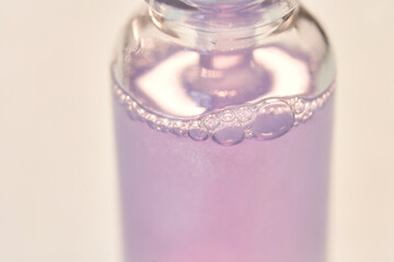 Close-up of a lavender-tinted liquid in a small glass bottle with bubbles floating on the surface.