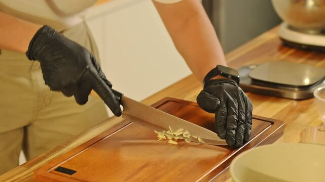 Close up of gloved hands cuts garlic on a wooden board