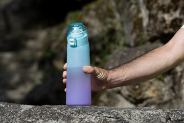 Man grabbing reusable flavored water bottle from rock for outdoor hydration and wellness use