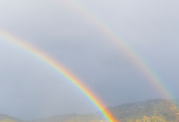 amazing bright rainbow in beautiful evening blue cloudy sky after rain and thunder with flash sun light streaming thruogh the clouds, weather thunderstorm concept