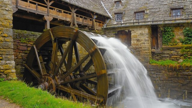 A water wheel with a wooden structure. It appears to be an old-fashioned mill or industrial piece, likely in Eastern Europe given the architectural style.