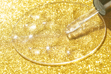 Skincare serum dropper with golden background and sparkling glitter highlights.