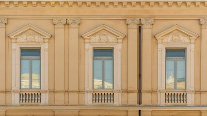 old yellow facade of house with three brown vintage wooden windows in retro italian european style