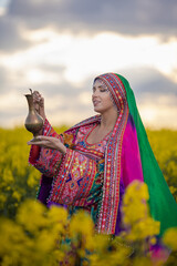Young woman in national Afghan costume dancing in a field with yellow rapeseed flowers