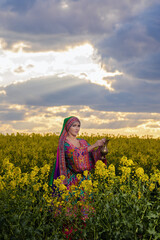 Fototapeta premium Young woman in national Afghan costume dancing in a field with yellow rapeseed flowers