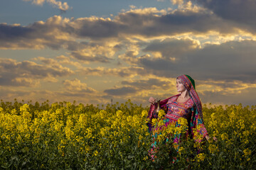 Young girl in national Afghan costume dancing in a field with yellow rapeseed flowers
