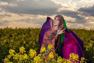 Young woman in national Afghan costume dancing in a field with yellow rapeseed flowers
