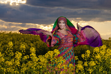 Young woman in national Afghan costume dancing in a field with yellow rapeseed flowers