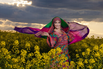 Young woman in national Afghan costume dancing in a field with yellow rapeseed flowers