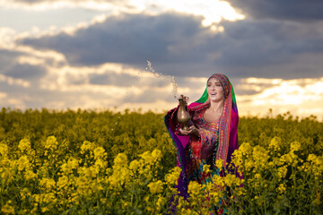 Young woman in national Afghan costume dancing in a field with yellow rapeseed flowers
