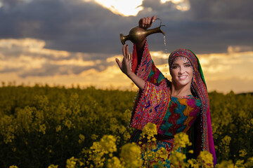 Young girl in national Afghan costume dancing in a field with yellow rapeseed flowers