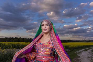 Young girl in national Afghan costume dancing in a field with yellow rapeseed flowers