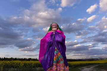 Young girl in national Afghan costume dancing in a field with yellow rapeseed flowers