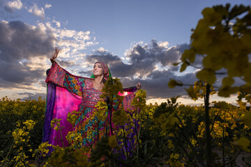 Young woman in national Afghan costume dancing in a field with yellow rapeseed flowers