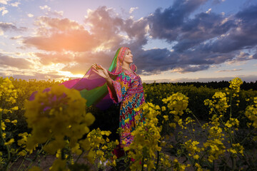 Young woman in national Afghan costume dancing in a field with yellow rapeseed flowers