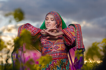 Young woman in national Afghan costume dancing in a field with yellow rapeseed flowers