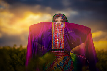 Young woman in national Afghan costume dancing in a field with yellow rapeseed flowers