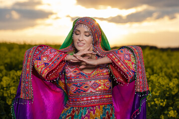 Young woman in national Afghan costume dancing in a field with yellow rapeseed flowers