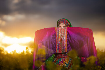Young woman in national Afghan costume dancing in a field with yellow rapeseed flowers