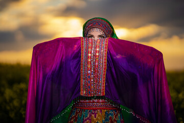 Young woman in national Afghan costume dancing in a field with yellow rapeseed flowers
