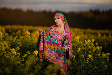 Young woman in national Afghan costume dancing in a field with yellow rapeseed flowers