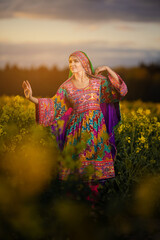 Young woman in national Afghan costume dancing in a field with yellow rapeseed flowers