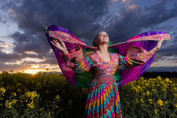 Young woman in national Afghan costume dancing in a field with yellow rapeseed flowers