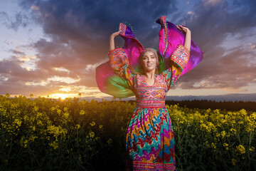 Young woman in national Afghan costume dancing in a field with yellow rapeseed flowers