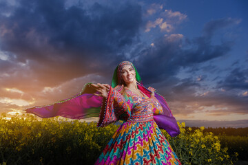 Fototapeta premium Young woman in national Afghan costume dancing in a field with yellow rapeseed flowers