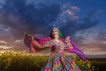 Young woman in national Afghan costume dancing in a field with yellow rapeseed flowers