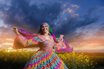 Young woman in national Afghan costume dancing in a field with yellow rapeseed flowers