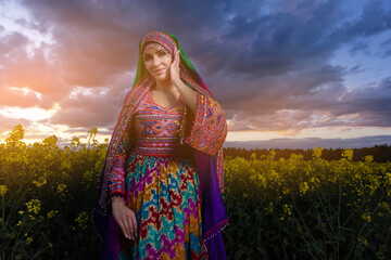 Young woman in national Afghan costume dancing in a field with yellow rapeseed flowers