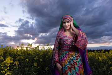 Young woman in national Afghan costume dancing in a field with yellow rapeseed flowers