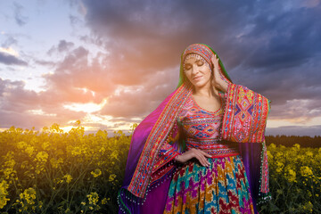 Young woman in national Afghan costume dancing in a field with yellow rapeseed flowers