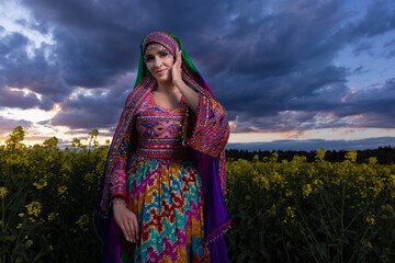Young woman in national Afghan costume dancing in a field with yellow rapeseed flowers