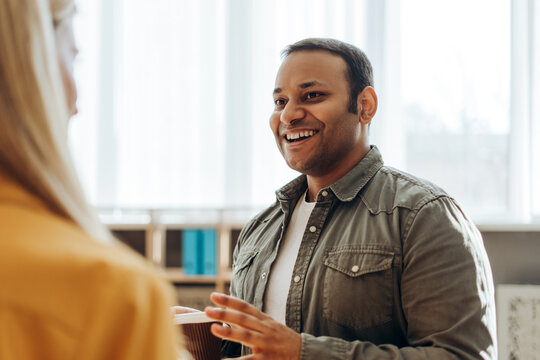 Indian businessman holding coffee cup talking with colleague in office