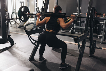 Athletic woman training with barbell in gym, back view