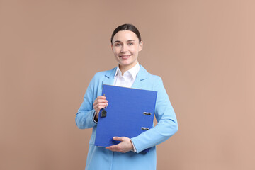 Real estate agent holding key with house shaped keychain and folder on beige background