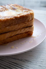 Close-up of buttered french toast with syrup and honey on pink plate