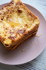 Close-up of buttered french toast with syrup and honey on pink plate