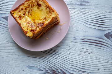 Close-up of buttered french toast with syrup and honey on pink plate